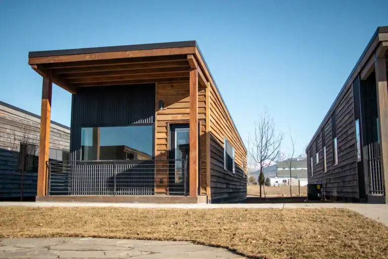 Modern wooden tiny home with a covered porch and large windows.