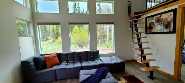 Bright interior of a tiny home featuring expansive windows and a cozy sectional sofa under the "Big sky".