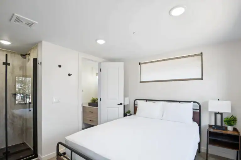 Bright bedroom with white walls, large window, and minimalist decor.