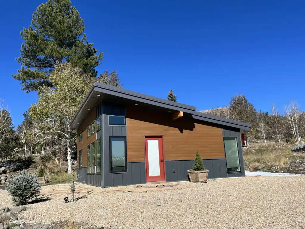 Contemporary tiny home with large windows and colorful door under a clear blue sky.