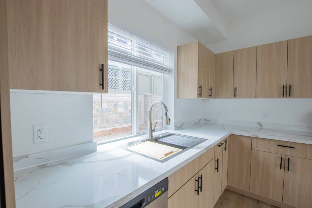 Efficient kitchen featuring natural wood cabinets, white marble countertops, and a large window for.