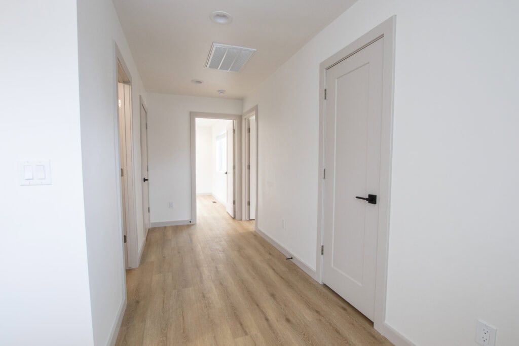 Bright hallway with white walls, wooden floors, and multiple doorways in a new home.