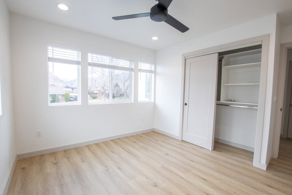 Bright, spacious room with large windows and ceiling fan.