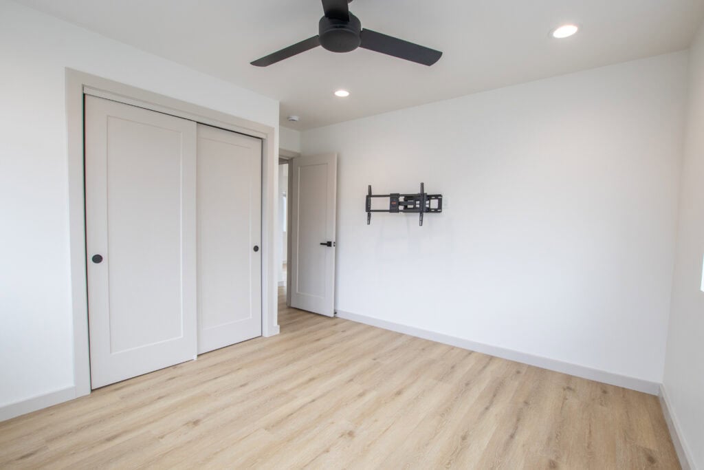 Modern bedroom with white walls, ceiling fan, and light wood flooring in Clyde Zip Kit Home.