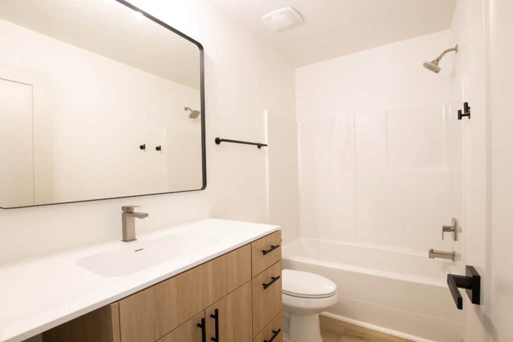 Bathroom with wooden vanity, white tiles, and modern fixtures in a Zip Kit Home.