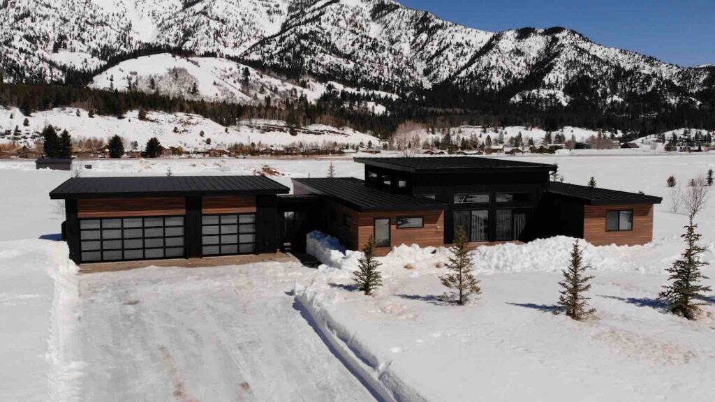Alpine Zip Kit Home with sleek black exterior and large windows, set against snowy mountains for a c.