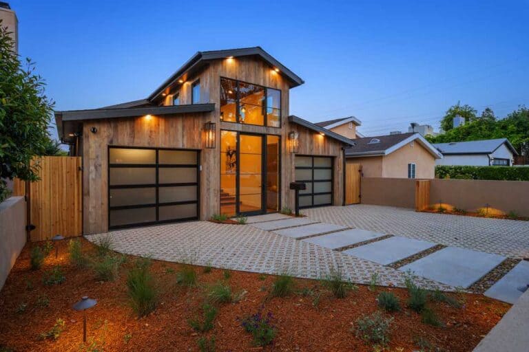 Modern barndominium-style home with wood siding, large glass entry, and two garage doors, with landscaped driveway and pathway.