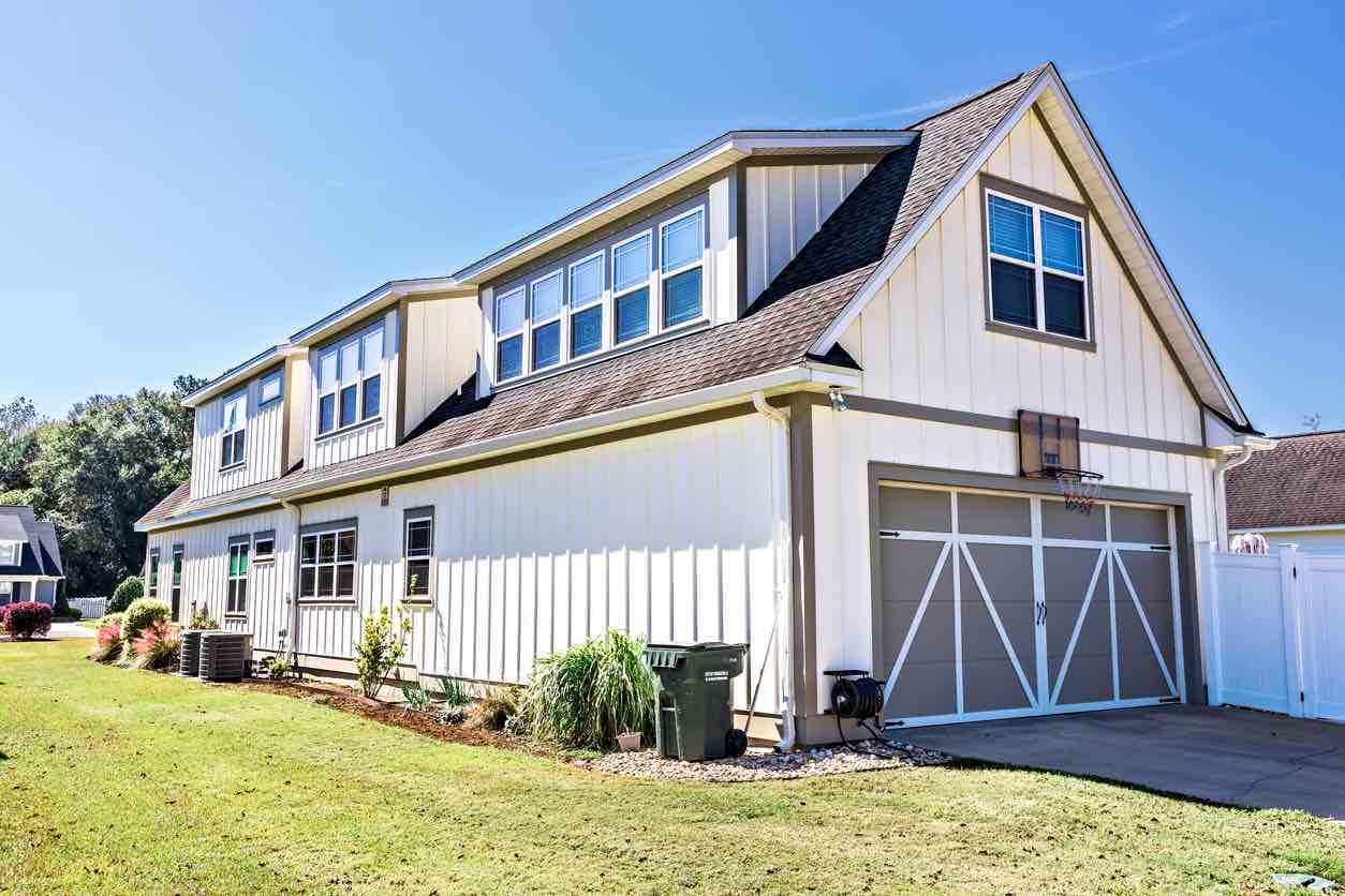 Two-story barndominium-style home with light vertical siding, gabled roof, and attached two-car garage with decorative doors.