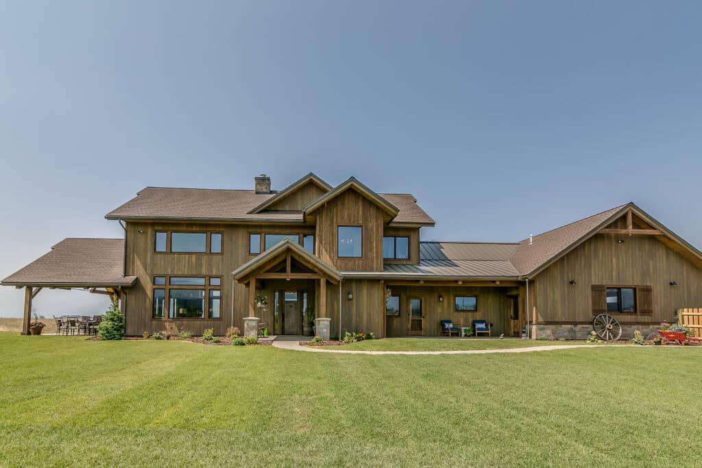 Rustic barndominium featuring a wooden exterior, large windows, and expansive lawn, ideal for custom.