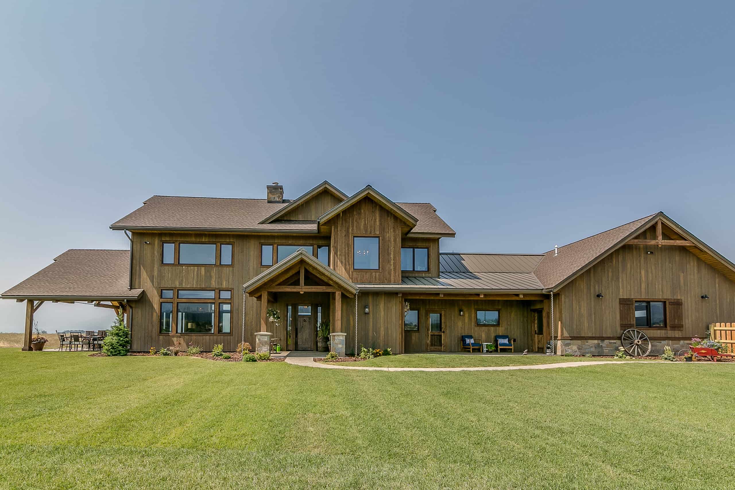 Rustic barndominium featuring a wooden exterior, large windows, and expansive lawn, ideal for custom.