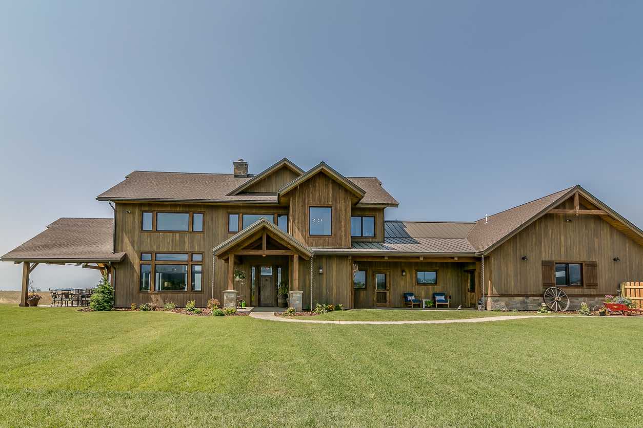 Rustic-modern barndominium-style home with wood siding, multiple gables, covered front entry, and attached garage wing.