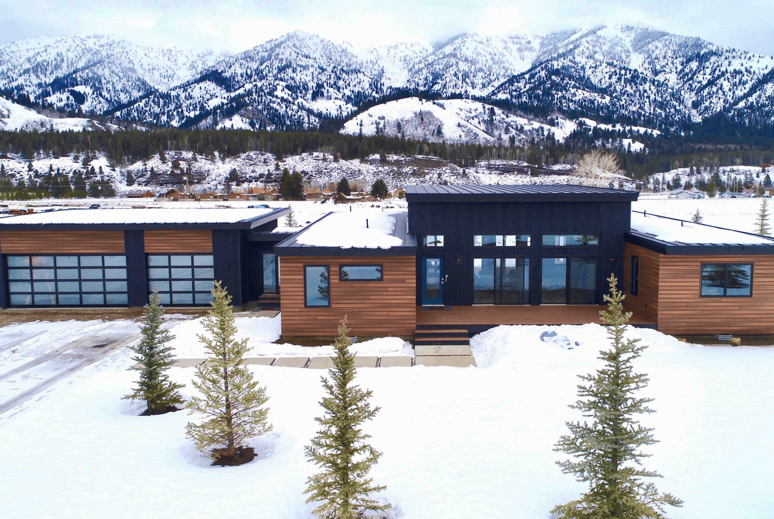 Alpine modern mountain home with wood siding, dark accents, and large windows set in a snowy landscape by Zip Kit Homes.