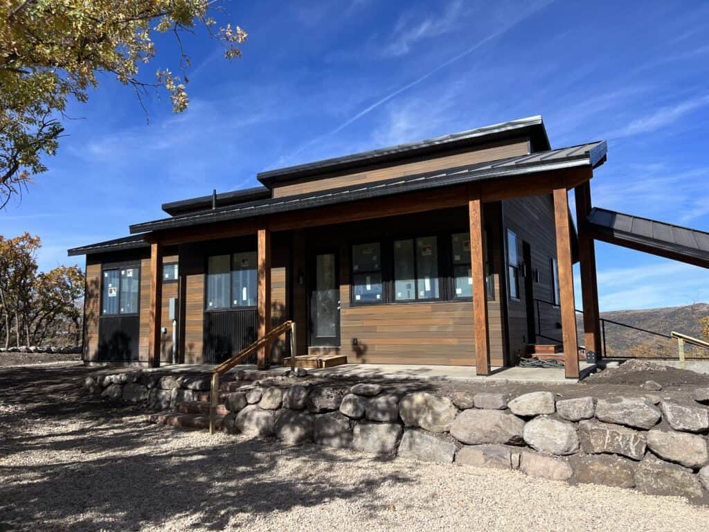 Moab model modern home exterior with covered front porch, wood siding, and stone retaining wall.