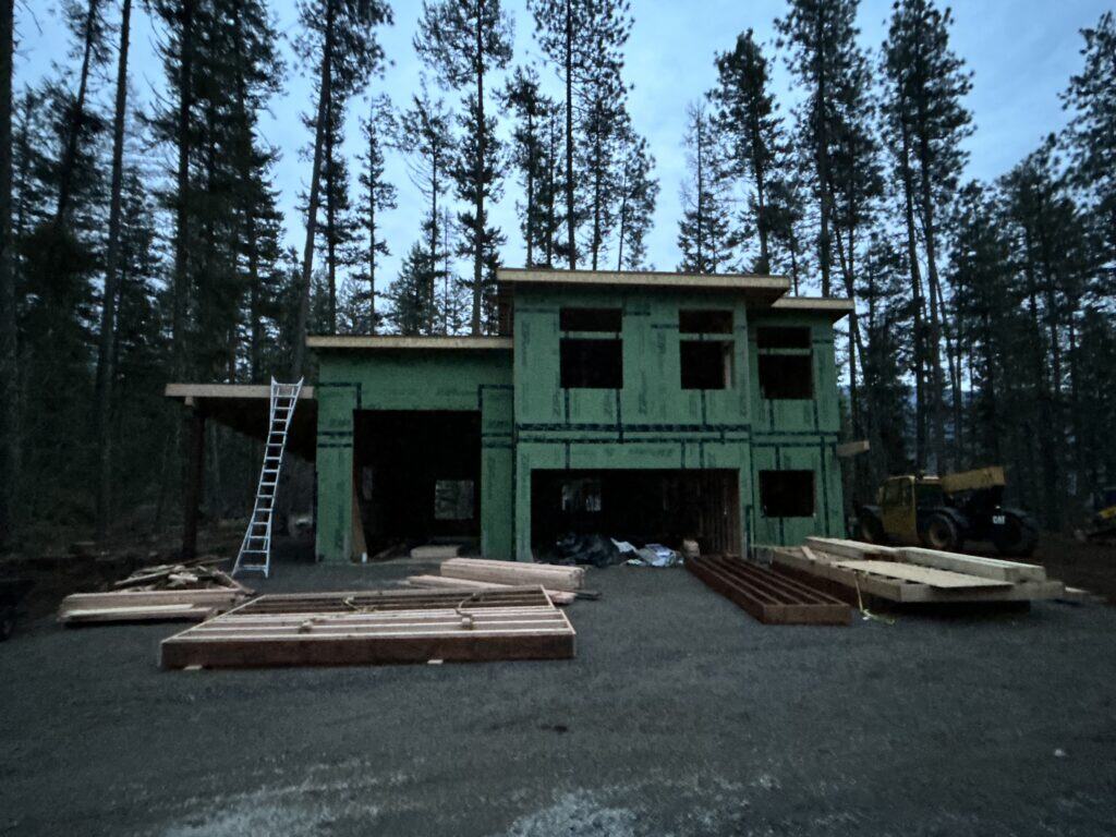 Contemporary Koda home being built in a wooded Idaho landscape with construction crew and modern architecture visible.