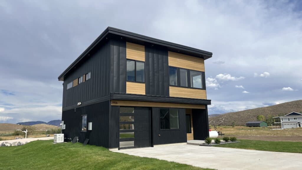 Modern two-story Bozeman home with black vertical siding, warm wood accents, and attached garage set in an open rural landscape