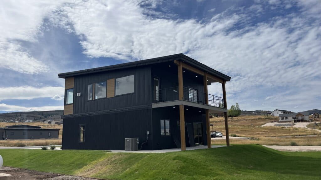 Bozeman two-story modern home with black metal siding, wood accents, and covered upper balcony.