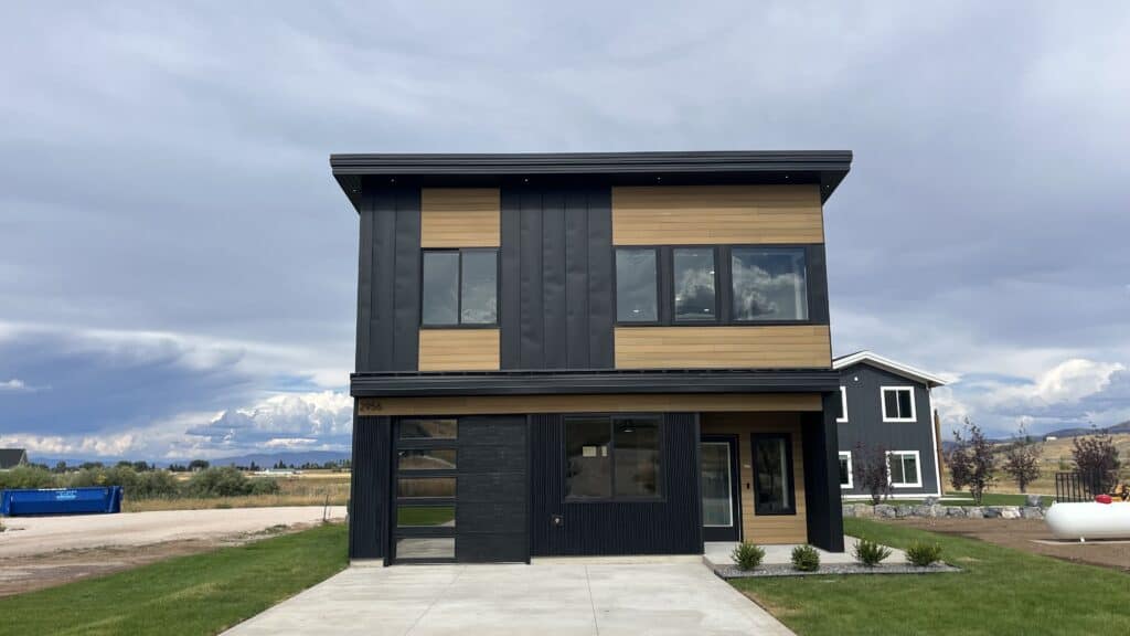 Bozeman two-story modern home with black metal siding, wood accents, and single-car garage viewed from the front.