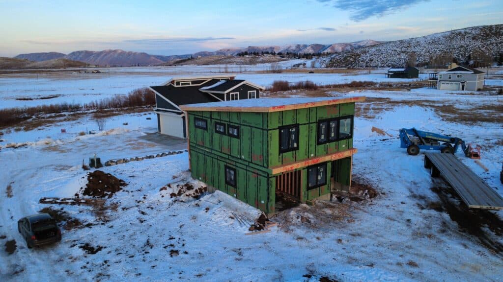 Green modular home under construction in snowy landscape near Bozeman.