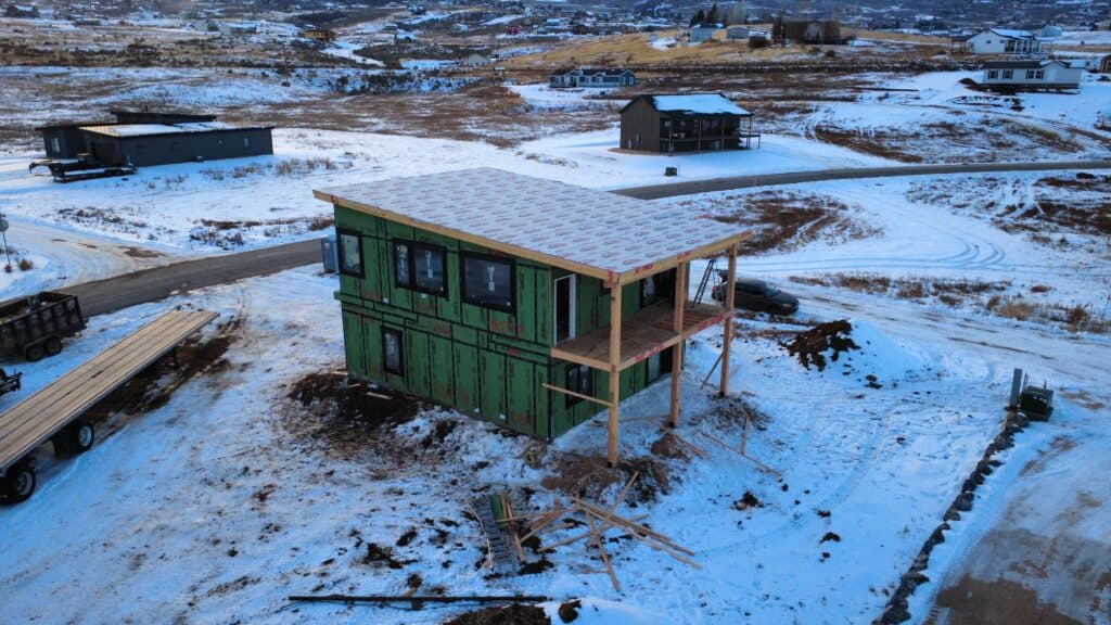 Under-construction green modular home in snowy landscape, Bozeman area.