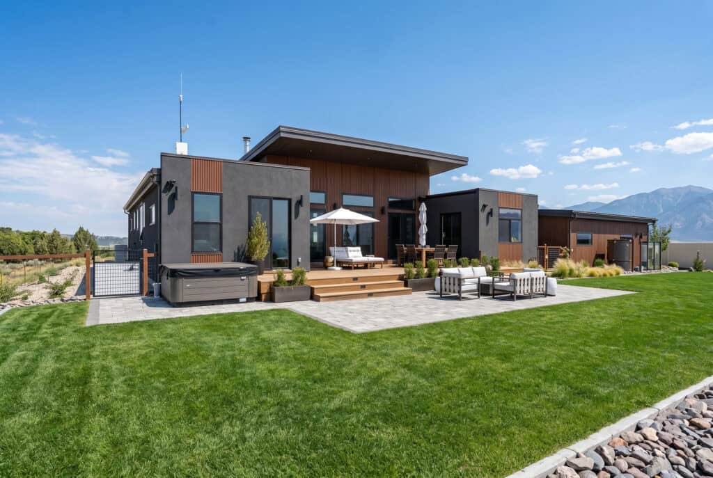 Alpine panelized home backyard with large patio, seating area, and large windows.