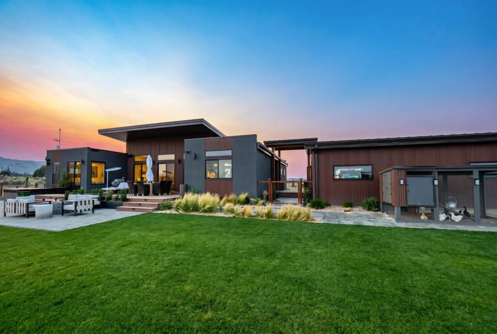 Alpine home rear elevation with patio seating, large lawn, and separate garage wing connected by breezeway.