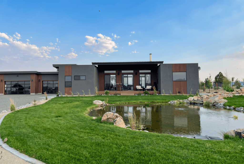 Alpine home front exterior with pond, landscaped approach, and full view of modern mountain design.