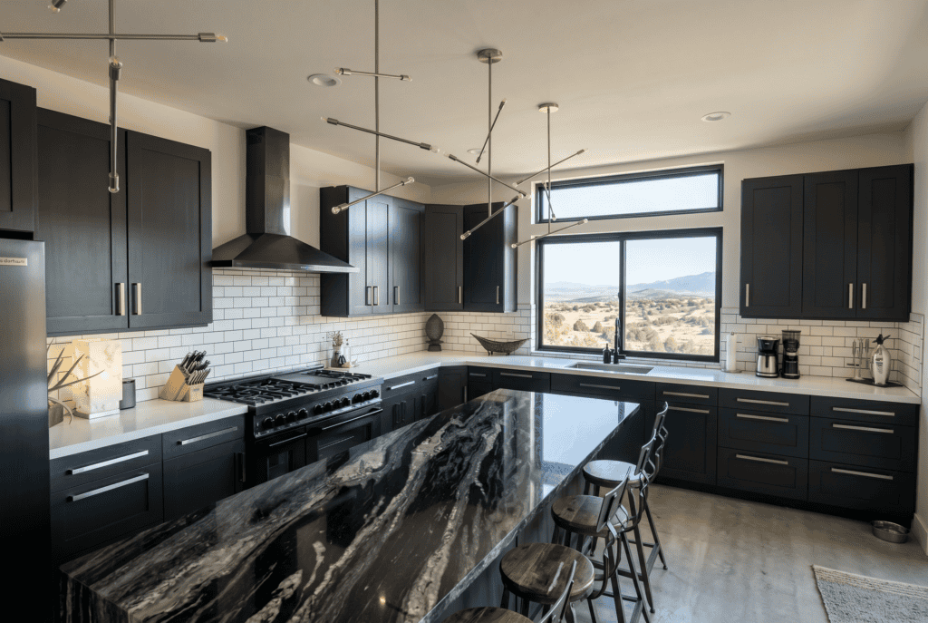 Modern black kitchen with large island, white subway tile backsplash, and mountain view through wind.