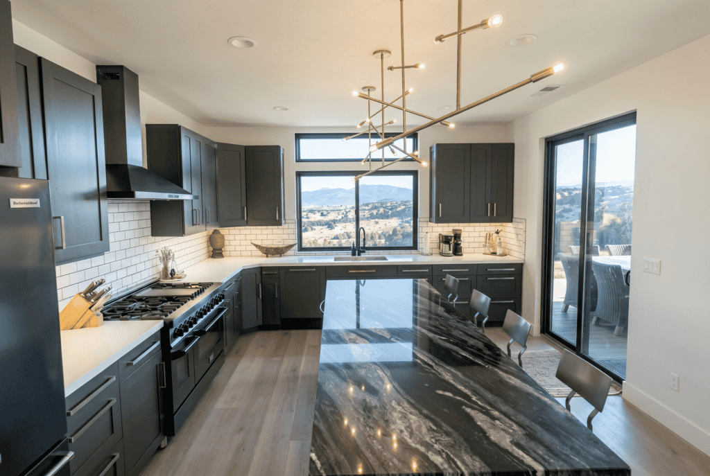 Modern kitchen with dark cabinetry, large island, and scenic mountain views through expansive window.
