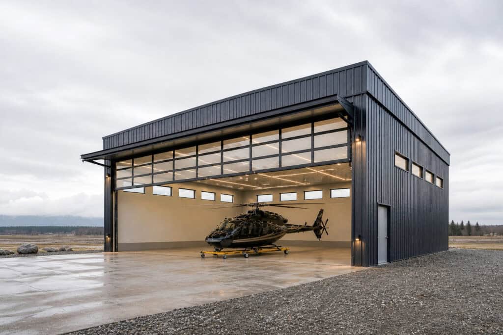 Modern aircraft hangar with large open doors and helicopter inside, durable metal construction.